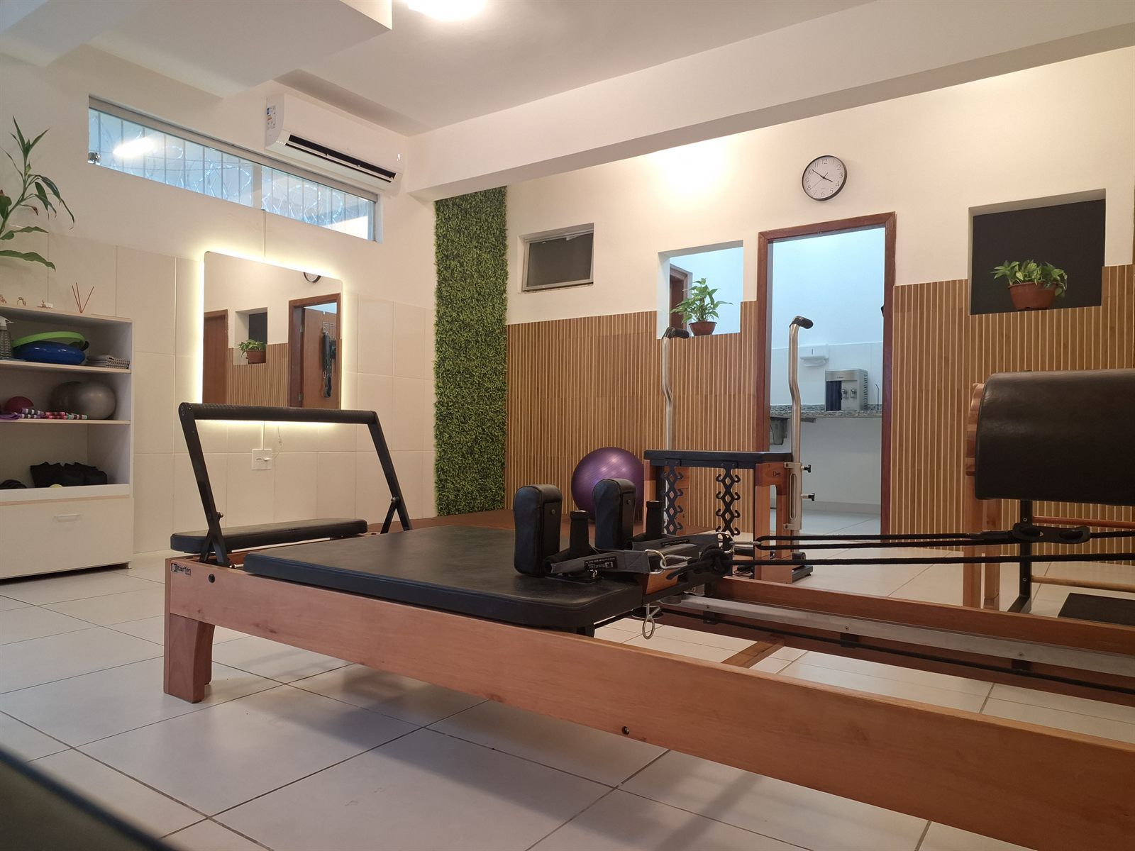 Sala de Pilates do Ipiranga com aparelho Reformer, espelhos iluminados e parede de madeira